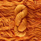 A pale orange skein of yarn lays vertically atop a bed of the same yarn with the strands running horizontally.