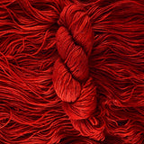 A deep cranberry red skein of yarn lays vertically atop a bed of the same yarn whose strands are laying horizontally.