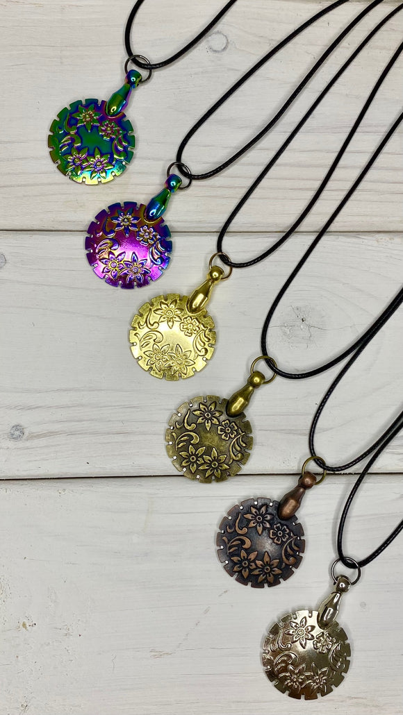 Circular pendants with concealed blade for cutting yarn on a simple necklace. Shown in 2 rainbow styles, gold, antique brass, copper and silver.