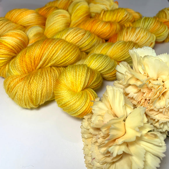 Four skeins of yellow variegated yarn with yellow chrysanthemums in the foreground