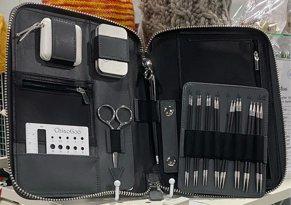 The Forte 2.0 Interchangeable Needle Set by ChiaoGoo are displayed in a black, zippered, faux leather case. On the left side of the inside of the case is a a white measuring tape, a tin of stitch markers, a pair of small scissors, and a gauge ruler and needle gauge. 
 In the centre is a black pen and a stainless still clip.  There is a faux leather card with a black elastic strap holding to the board various sized tips made from a blend of stainless steel and either Carbon Fiber or African Blackwood.  