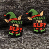 Two silicone stitch stoppers which say What the Elf? in green, beige, and red lettering on a black background.  Atop the lettering is a green elf hat with a red bauble on the end and a red band around the bottom.  Pointed elf ears are beside the hat.  Red legs wearing green pointed shoes comes out of the bottom of the lettering.  