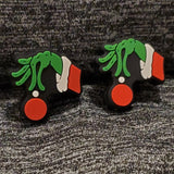 Two silicone stitch stoppers in the shape of a green grinchy hand at the end of a Santa suited arm holding a red Christmas ball.  