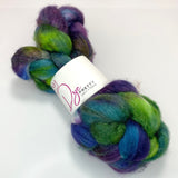 A braid of dyed wool top is cinched at the middle in a white label reading Dye Pretty Yarn + Fibre.  The fibre is dyed royal blue, purple, neon and dark green and the braid sits atop a white background.