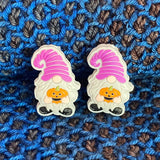 Two silicone stitch stoppers in the form of gnomes. The gnomes are wearing purple striped hats and black shoesr.  They have grey beards and are holding jack-o-lanterns in their hands.  