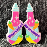 Two silicone stitch stoppers in the form of hot sauce bottles.  The bottles are hot pink with pale blue lids and labels.  White diamond shaped "sparkles" adorn the top of the bottle.  A pale pink banner is draped across the bottle with the word "Neurospicy" emblazoned on it.  A yellow and an orange pepper also adorn each bottle.  