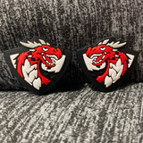 Two silicone stitch stoppers in the form of triangular crests with a red dragon in the centre and coming out the top of the triangle.  The dragon is against a white background bordered in black.  