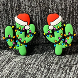 Two silicone stitch stoppers in the form of green cactuses wearing Santa hats and wrapped in multicoloured Christmas lights.  