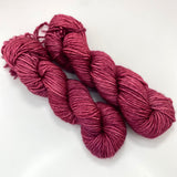 Two mini skeins of deep pink tonal worsted weight yarn. 