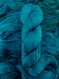 A skein of yarn sits vertically atop a bed of the same yarn laid out with the strands running horizontally.  The yarn is all a tonal greenish teal colour.  